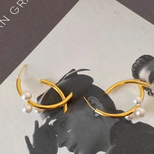 Gros plan de boucles d'oreilles en C dorées avec trois perles blanches lustrées