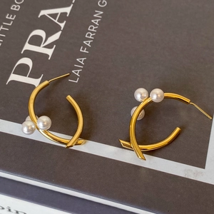 Détail de boucles d'oreilles C dorées avec motif croisé et trois perles blanches