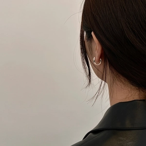 Close-up of a minimalist silver hoop earring worn by a model in black leather jacket
