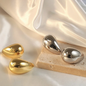 Polished gold and silver teardrop earrings displayed on elegant silk and travertine