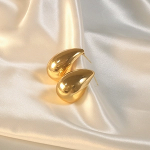 Close-up of teardrop earrings with gold mirror finish on a satin fabric background