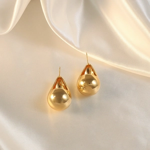 Close-up of golden teardrop hollow earrings on soft beige silk fabric background