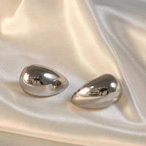 Macro detail of teardrop earrings with mirror-polished silver finish on silk fabric