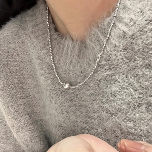 Macro detail of silver beaded necklace chain with metallic pendant on grey sweater