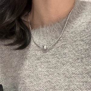 Close-up of minimalist silver pearl necklace featuring a polished bead on a knitted sweater