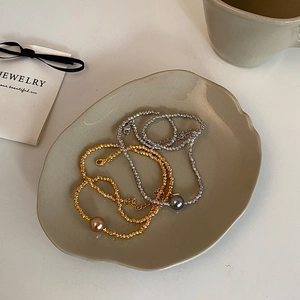 Detail showing gold and silver bead necklaces with large center pearls on a ceramic tray
