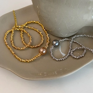 Irregular metal beaded necklace with large champagne and grey pearls on ceramic tray