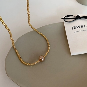Detailed close-up of a golden textured twist chain necklace with a brown pearl pendant