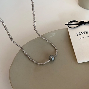 Detail view of fine metallic silver beads with a central dark grey lustrous pearl necklace