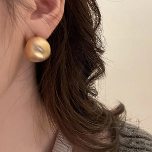 Dettaglio macro di un orecchino a chicco ricurvo in oro opaco minimalista sull'orecchio