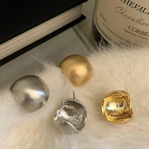 Vista macro di orecchini a lobo curvi opachi in oro e argento su sfondo peluche