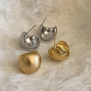 Dettaglio macro di orecchini a perno curvi in oro e argento opaco su tessuto felpato