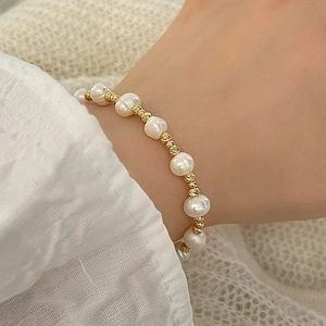Détail macro d'un bracelet en perles d'eau douce avec perles dorées ciselées au poignet
