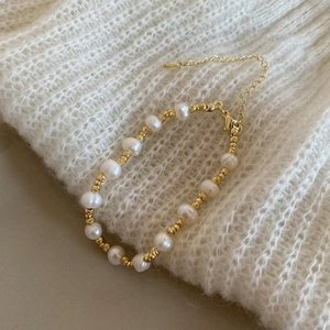 Détail d'un bracelet en perles et perles dorées posé sur une maille blanche douce