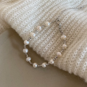 Détail d'un bracelet en perles d'eau douce et billes argentées sur un pull en maille