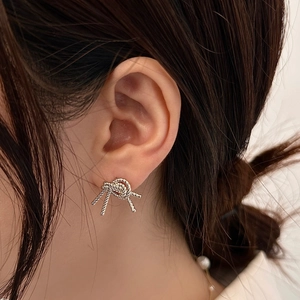 Close-up of silver knot stud earrings with woven texture on model for a refined look