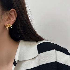 Close-up of elegant gold knot earrings with textured finish on a female model
