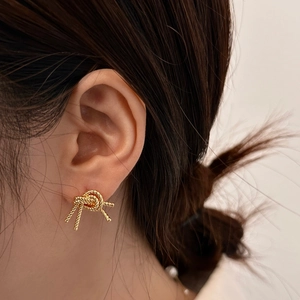 Detailed view of elegant gold-plated knot stud earrings worn by a female model
