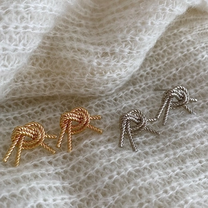 Detailed close-up of gold and silver knot-style earrings on a white knit sweater background