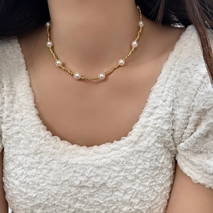 Gros plan d'un collier de perles dorées et blanches porté sur le cou d'un mannequin