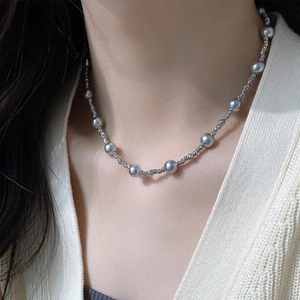 Gros plan d'un collier de perles avec chaîne en métal sur un cardigan en maille blanc