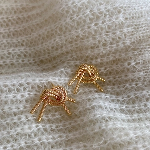 Macro shot of gold double-layered knot stud earrings on a soft white knit background