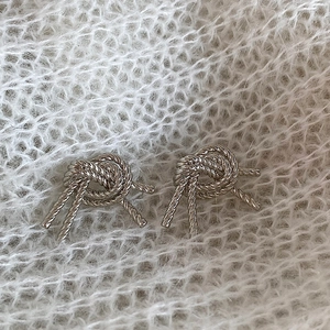 Close-up of twisted love knot stud earrings with silver texture on soft white knit fabric