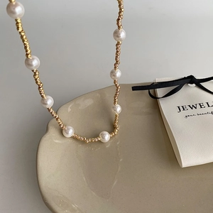 Gros plan d'un collier de perles dorées et perles blanches sur plateau céramique