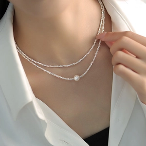 Close-up of double-layered silver-tone necklace featuring a central white pearl detail