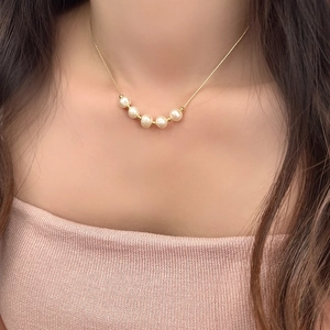 Detail of freshwater pearl necklace with gold beads on thin snake chain worn by a model