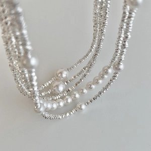 Layered necklace with white pearls and faceted silver beads on a clean background
