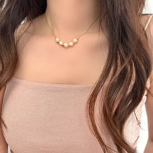Detail of 5 freshwater pearls on a gold-plated necklace worn by a model in soft light