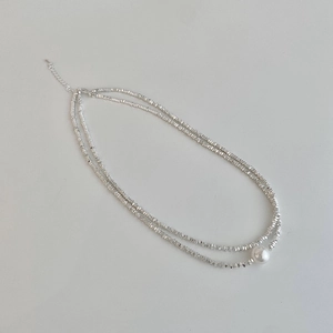 Detail showing double-layer silver bead necklace with a large white pearl and lobster clasp