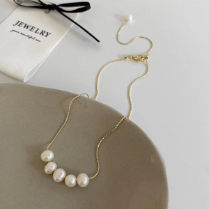 Macro detail of five freshwater pearls on a gold chain over a ceramic plate