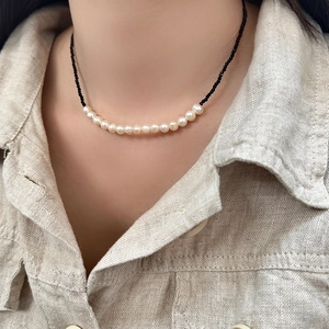 Close-up of minimalist freshwater pearl necklace with black crystals on linen fabric