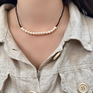 Minimalist freshwater pearl and black crystal necklace on a beige linen shirt model