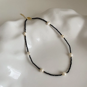 Detail of freshwater pearl and black crystal necklace on white ceramic tray