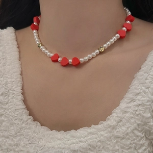 Détail d'un collier de perles avec cœurs rouges et smileys dorés porté par un mannequin