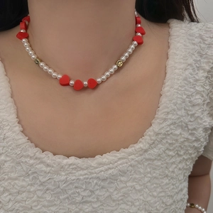 Gros plan d'un collier de perles avec cœurs rouges et visages souriants dorés porté