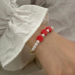 Détail d'un bracelet de perles avec cœurs rouges porté sur une manche à volants blancs