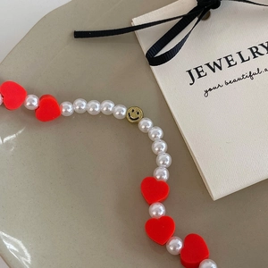 Détail du collier de perles avec cœur rouge et pendentif smiley doré sur un plateau de présentation