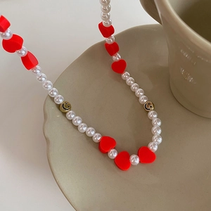 Détail du collier de perles avec cœurs rouges et perles dorées sur plateau céramique