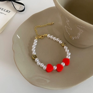 Détail du bracelet en perles avec breloques cœur rouge et perles smiley dorées sur un plateau
