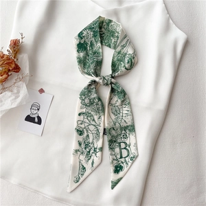 Détail d'un foulard étroit en soie avec lettre B et imprimé floral vert noué au décolleté