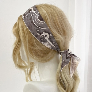 Détail d'un foulard en soie étroit double-face noué en bandeau sur cheveux blonds
