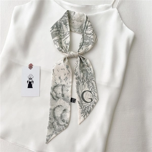 Détail d'un foulard étroit beige avec imprimé floral et lettre G noire sur un haut en soie