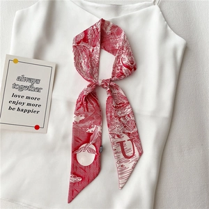 Détail d'un foulard étroit en soie Toile de Jouy rouge noué en nœud sur un haut