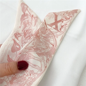 Gros plan d'un foulard étroit en soie avec motifs floraux bordeaux et lettre H