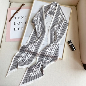 Close-up of a narrow silk scarf with black and white geometric patterns and accessories