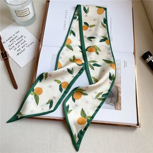 Flat lay of narrow floral silk scarf with orange prints on fashion magazine and accessories